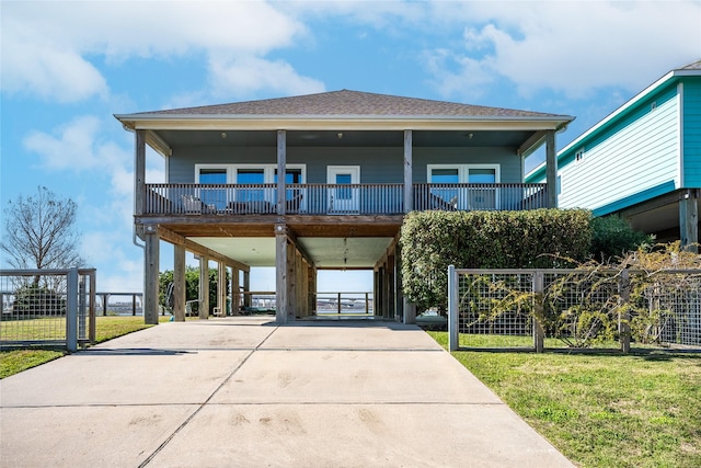 coastal home featuring driveway, fence, a front lawn, and a carport