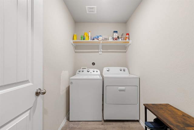 clothes washing area with light wood-style flooring, laundry area, visible vents, baseboards, and washing machine and clothes dryer