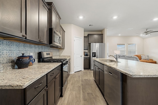 kitchen featuring appliances with stainless steel finishes, light wood-style floors, open floor plan, a sink, and an island with sink