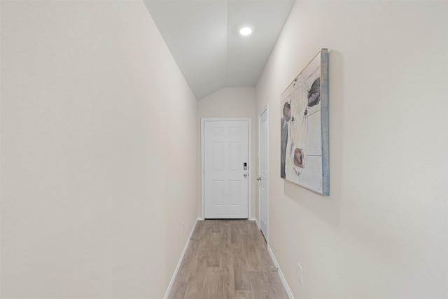 corridor featuring light wood-type flooring, baseboards, and vaulted ceiling