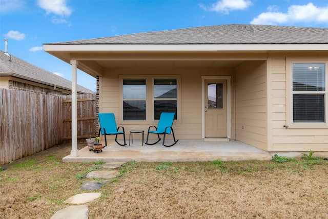 property entrance featuring a shingled roof, a patio area, and fence