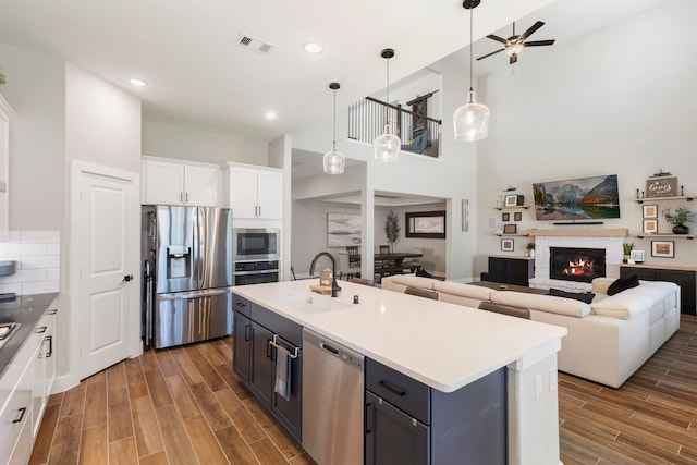 kitchen featuring light countertops, appliances with stainless steel finishes, white cabinets, a sink, and an island with sink