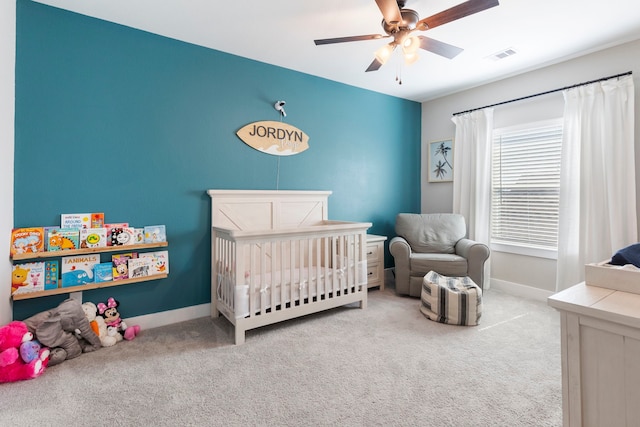 bedroom with visible vents, a ceiling fan, carpet flooring, a crib, and baseboards