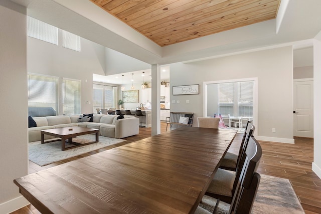 dining space featuring wooden ceiling, wood finished floors, a towering ceiling, baseboards, and a tray ceiling