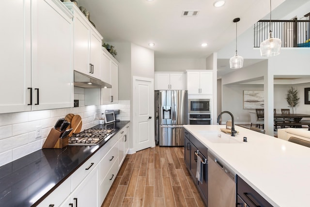 kitchen with stainless steel appliances, a sink, white cabinets, and under cabinet range hood