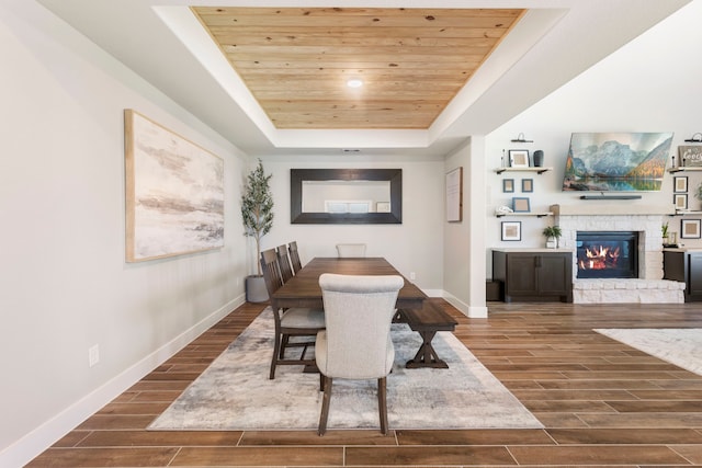 dining area featuring baseboards, a raised ceiling, wood ceiling, wood tiled floor, and a fireplace