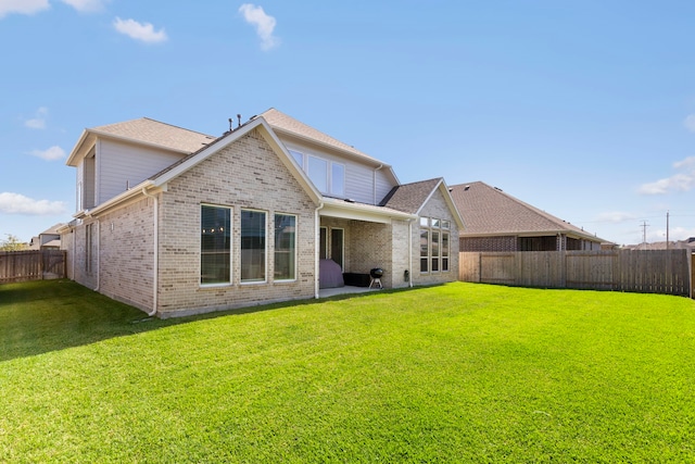 rear view of property featuring brick siding, a lawn, and a fenced backyard