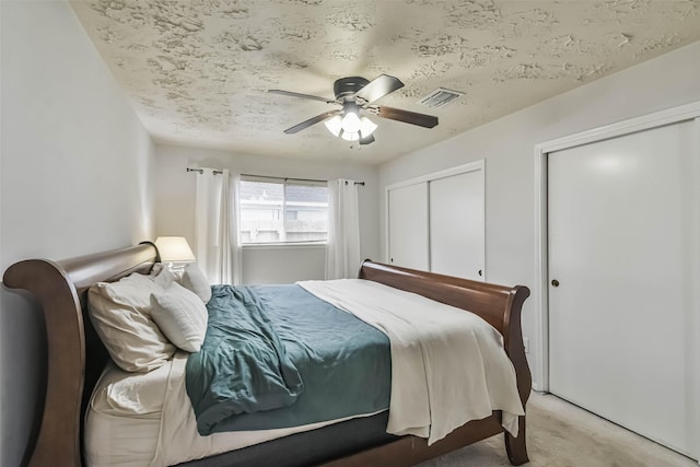 bedroom with two closets, visible vents, a ceiling fan, light carpet, and a textured ceiling