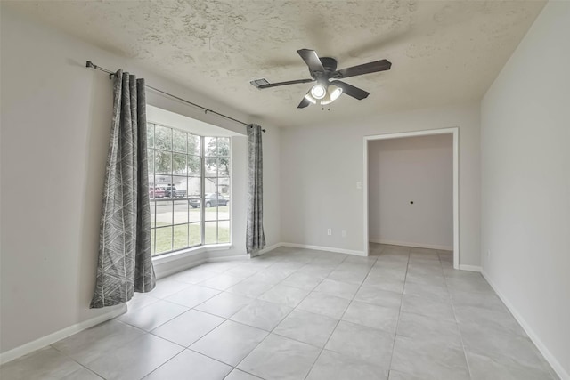 empty room featuring light tile patterned floors, baseboards, a ceiling fan, and a textured ceiling