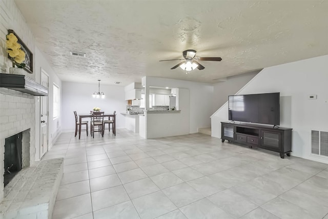 living room with ceiling fan with notable chandelier, a textured ceiling, a brick fireplace, and visible vents