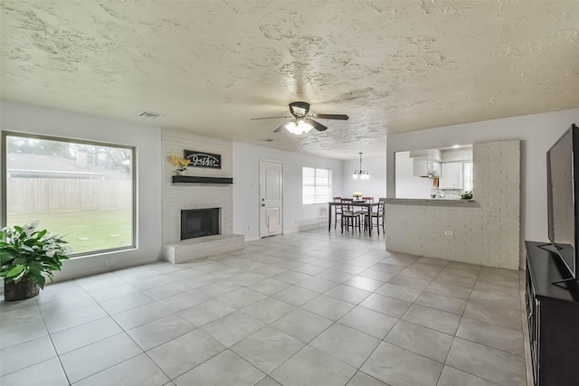 unfurnished living room featuring visible vents, a ceiling fan, a textured ceiling, a fireplace, and light tile patterned flooring