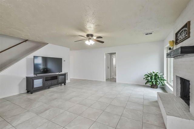 living area featuring a textured ceiling, ceiling fan, light tile patterned floors, visible vents, and a brick fireplace