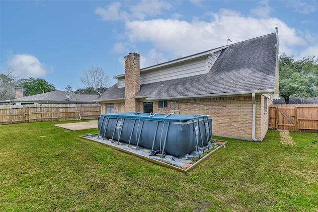 back of house featuring a shingled roof, a fenced in pool, a fenced backyard, a yard, and brick siding