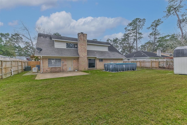 rear view of house with brick siding, a lawn, a fenced in pool, a chimney, and a patio area