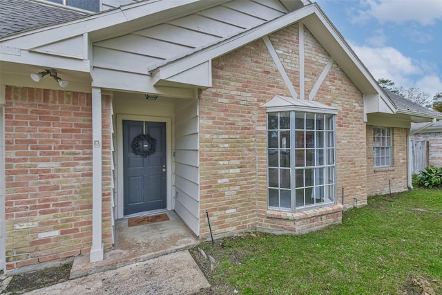 property entrance featuring a yard, brick siding, and roof with shingles