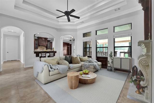 living room featuring light tile patterned floors, visible vents, a tray ceiling, and arched walkways