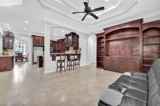 living area with arched walkways, ceiling fan, a raised ceiling, and crown molding