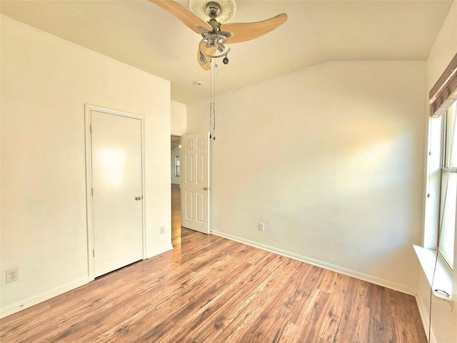 empty room featuring vaulted ceiling, wood finished floors, a ceiling fan, and baseboards