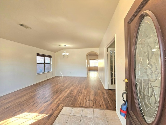 spare room with arched walkways, a chandelier, visible vents, baseboards, and light wood-style floors