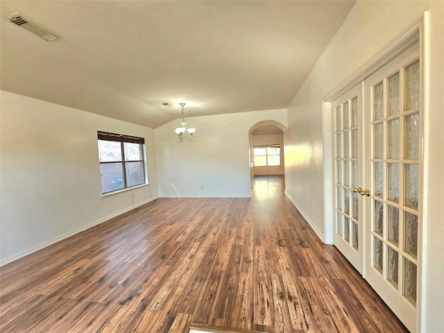 empty room featuring arched walkways, lofted ceiling, a chandelier, dark wood-style flooring, and visible vents