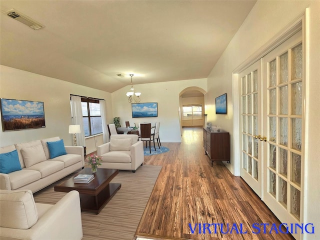 living room with arched walkways, visible vents, an inviting chandelier, vaulted ceiling, and wood finished floors