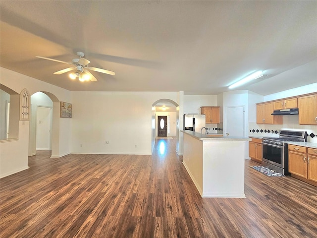 kitchen with under cabinet range hood, arched walkways, stainless steel appliances, and open floor plan