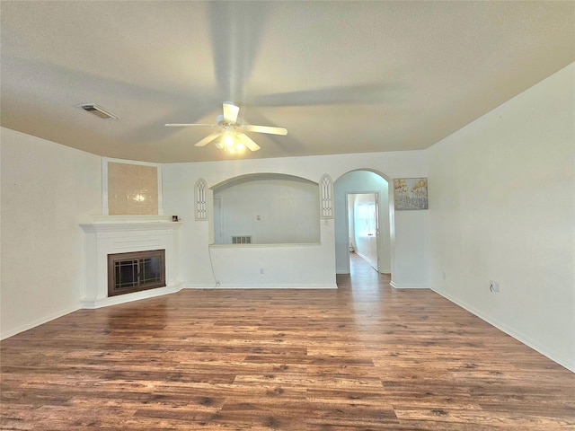 unfurnished living room with a ceiling fan, a glass covered fireplace, visible vents, and wood finished floors