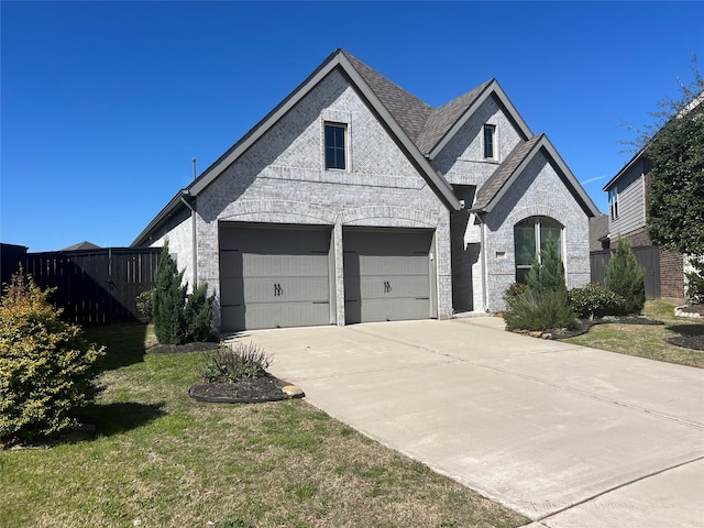 french provincial home with brick siding, a shingled roof, driveway, and fence