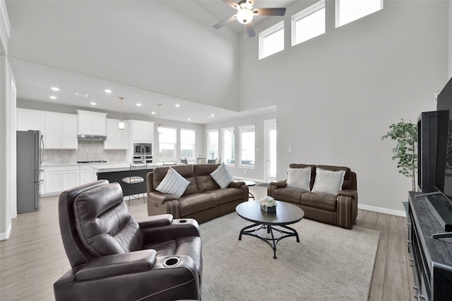 living room with ceiling fan, recessed lighting, a high ceiling, baseboards, and light wood finished floors