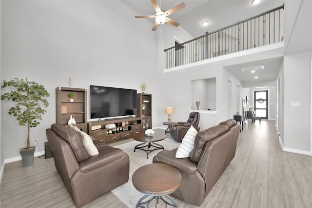 living area with ceiling fan, a high ceiling, wood finished floors, and baseboards