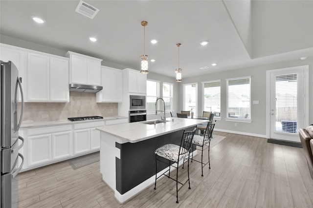 kitchen featuring under cabinet range hood, a sink, visible vents, appliances with stainless steel finishes, and tasteful backsplash