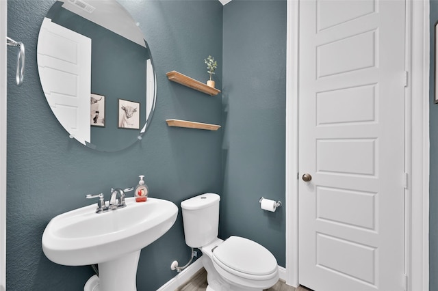 bathroom with a textured wall, baseboards, a sink, and toilet