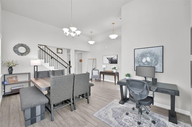 office area with a towering ceiling, light wood-style floors, baseboards, and a chandelier