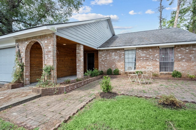 view of front of home with a garage, a patio, brick siding, and a shingled roof