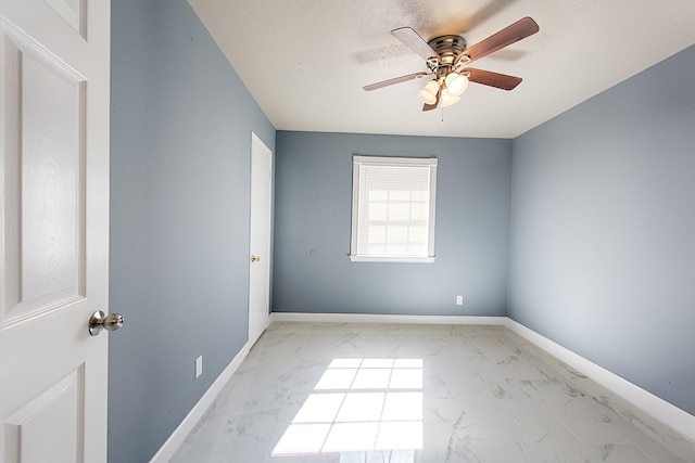 empty room with marble finish floor, a ceiling fan, and baseboards