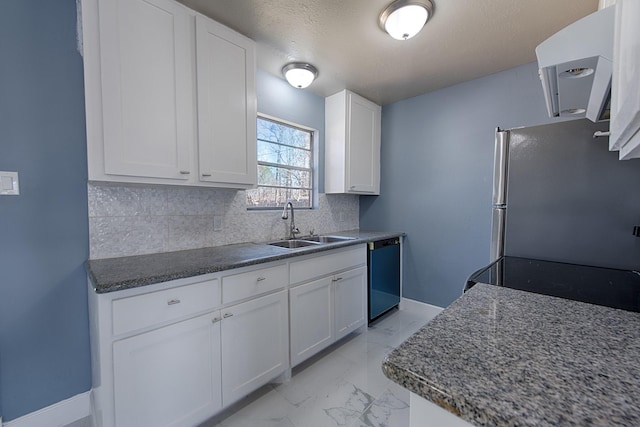 kitchen featuring dishwashing machine, a sink, marble finish floor, backsplash, and freestanding refrigerator