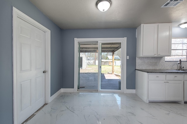 interior space featuring marble finish floor, visible vents, backsplash, white cabinetry, and baseboards