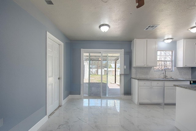 kitchen featuring marble finish floor, visible vents, backsplash, a sink, and baseboards