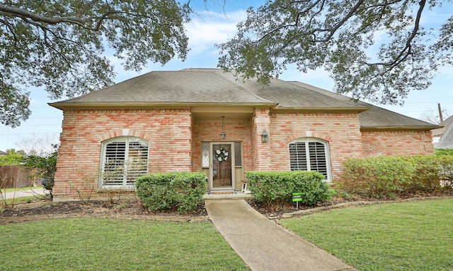 view of front of property featuring brick siding, a front lawn, and a shingled roof