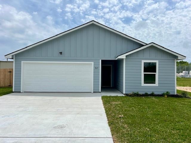 809 Flycatcher Dr, Palacios, TX 77465 - ranch-style house with driveway, an attached garage, a front lawn, and board and batten siding