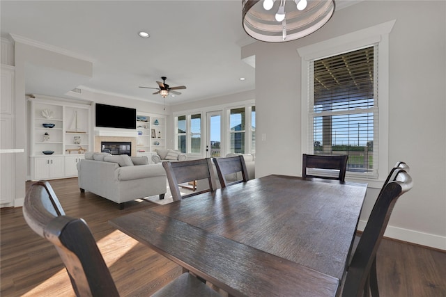 dining room with ceiling fan, baseboards, ornamental molding, dark wood-style floors, and a glass covered fireplace