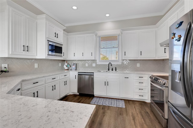 kitchen with stainless steel appliances, a sink, white cabinets, ornamental molding, and wall chimney exhaust hood