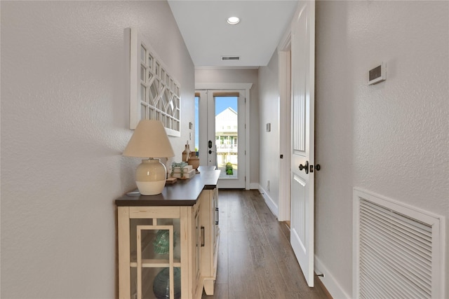 doorway featuring visible vents, a textured wall, baseboards, and wood finished floors