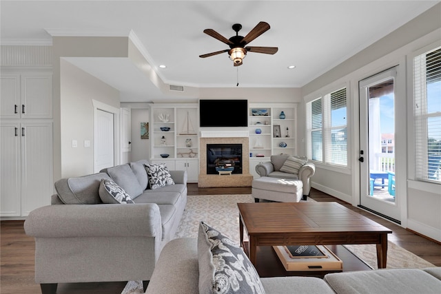 living room with ceiling fan, a premium fireplace, wood finished floors, visible vents, and crown molding