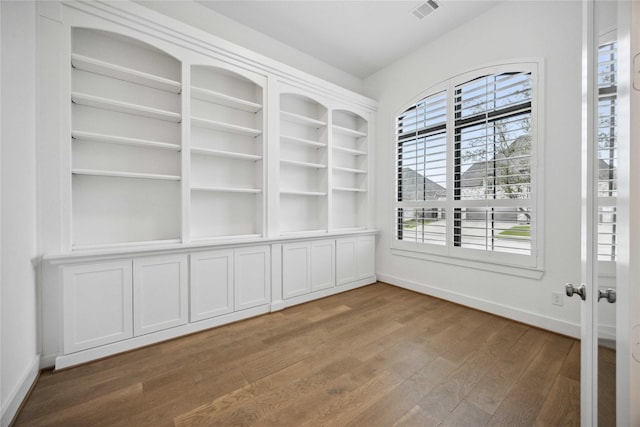 empty room featuring baseboards, wood finished floors, and visible vents