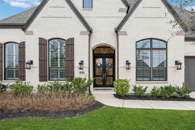 property entrance featuring brick siding, a shingled roof, and french doors