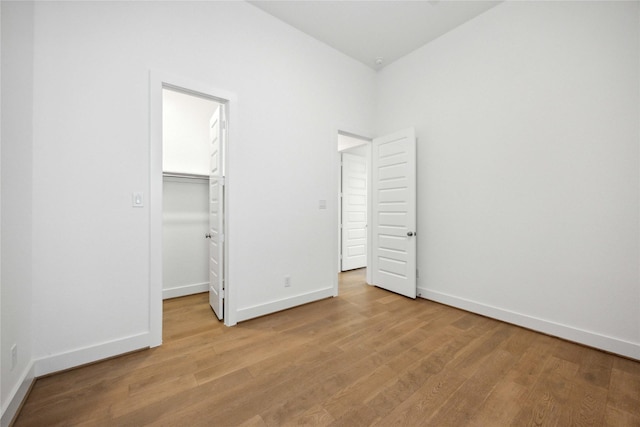 unfurnished bedroom featuring a walk in closet, light wood finished floors, and baseboards