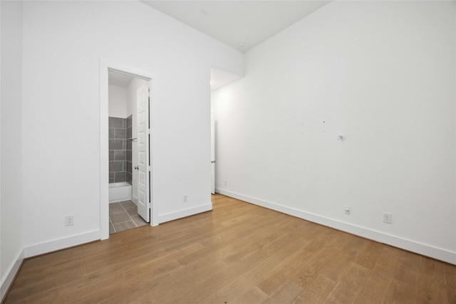 unfurnished bedroom with ensuite bathroom, baseboards, and light wood-style floors