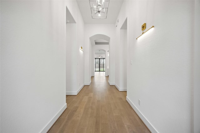 hall featuring light wood-type flooring, baseboards, arched walkways, and a notable chandelier