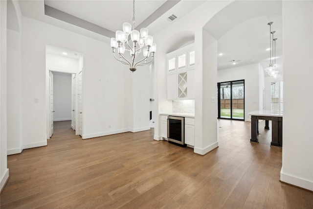 unfurnished living room with beverage cooler, an inviting chandelier, visible vents, a dry bar, and light wood-style flooring